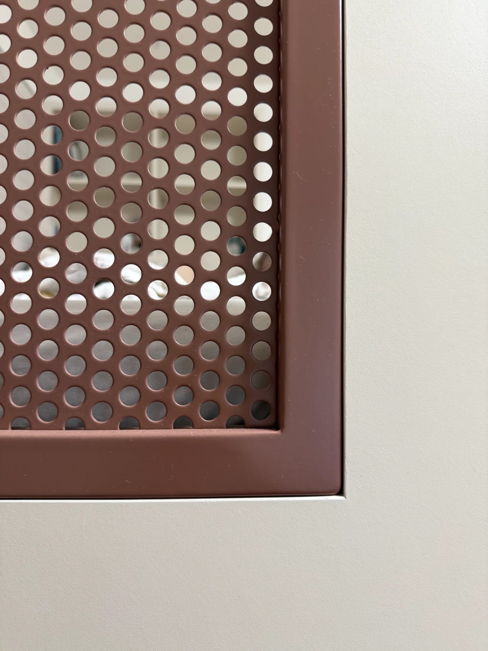 Hnědá perforovaná kovová deska s bílým povrchem.